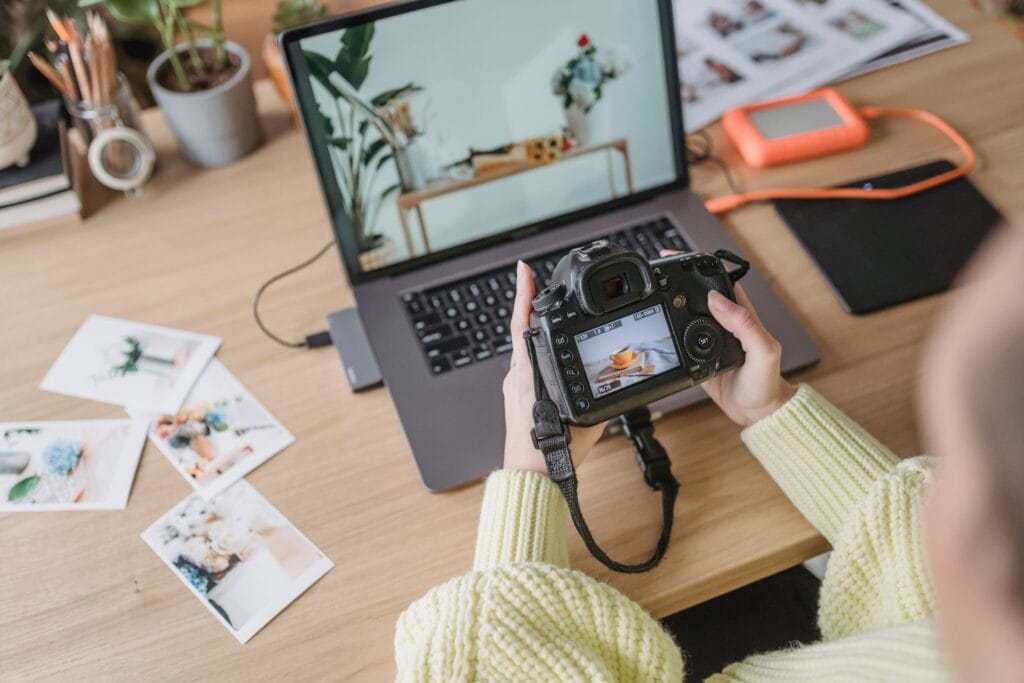 Kreativschaffende kuratiert Projekte für die eigene Portfolio-Website mit Kamera, Laptop und Ausdrucken