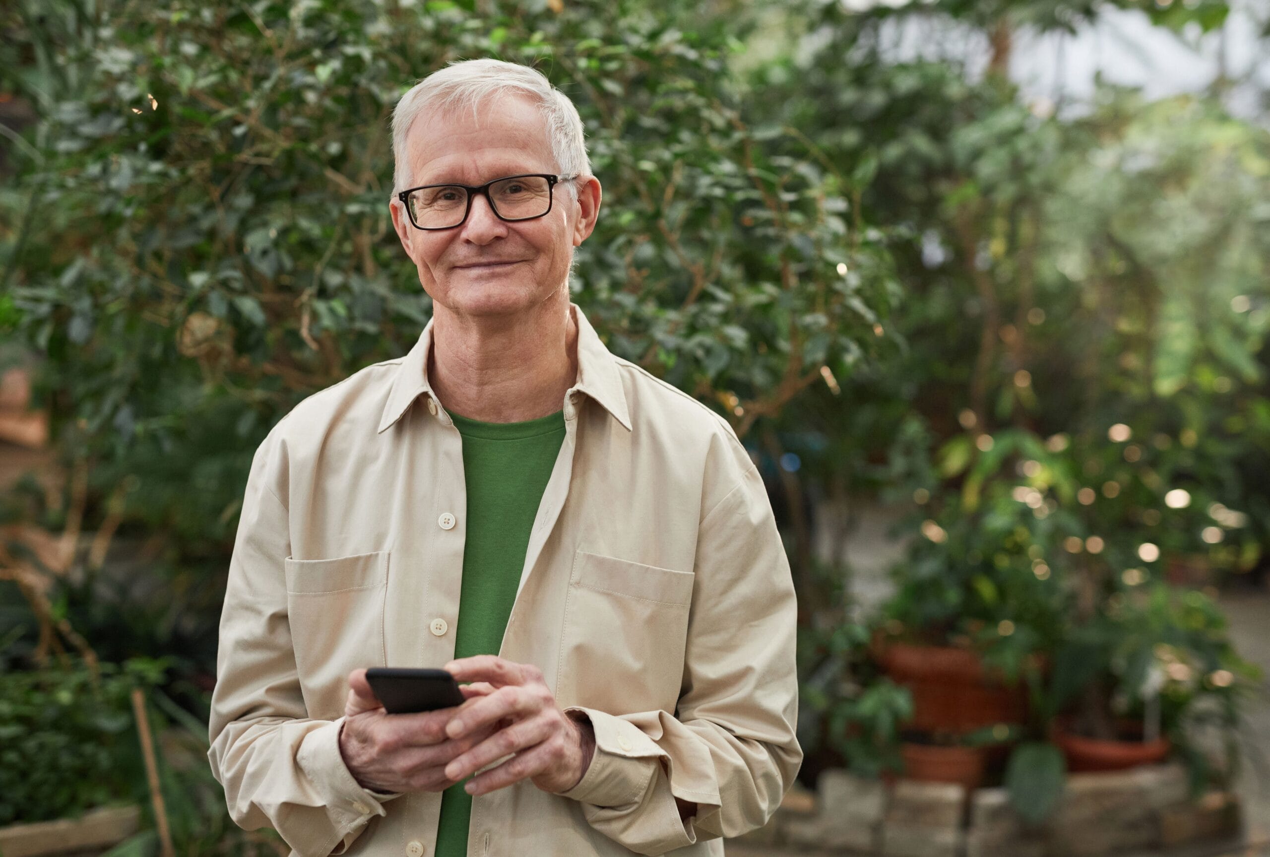 Älterer Mann nutzt selbstbewusst sein Smartphone im Garten – Sinnbild für digitale Kompetenz im Alter