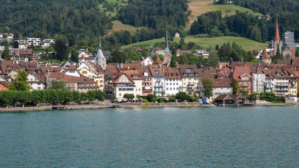 Die Zuger Altstadt vom Zugersee aus gesehen, mit Zytturm und Kirchturm vor den bewaldeten Hängen des Zugerbergs